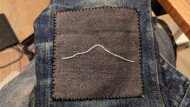 The outline of a mountain that may or may not be recognizable to someone, stitched as a single line with thick white thread onto a black denim patch. The patch is rimmed with a tidy blanket stitch in thick black thread and affixed to my blue jeans with a whip stitch that almost completely blends in with the blanket stitch.